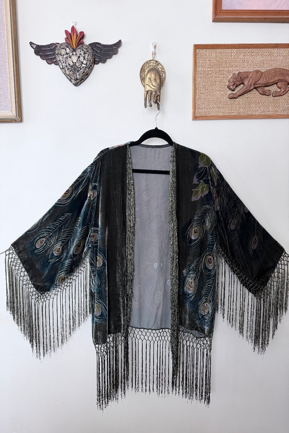 Green velvet silk jacket with peacock feathers on a white wall.
