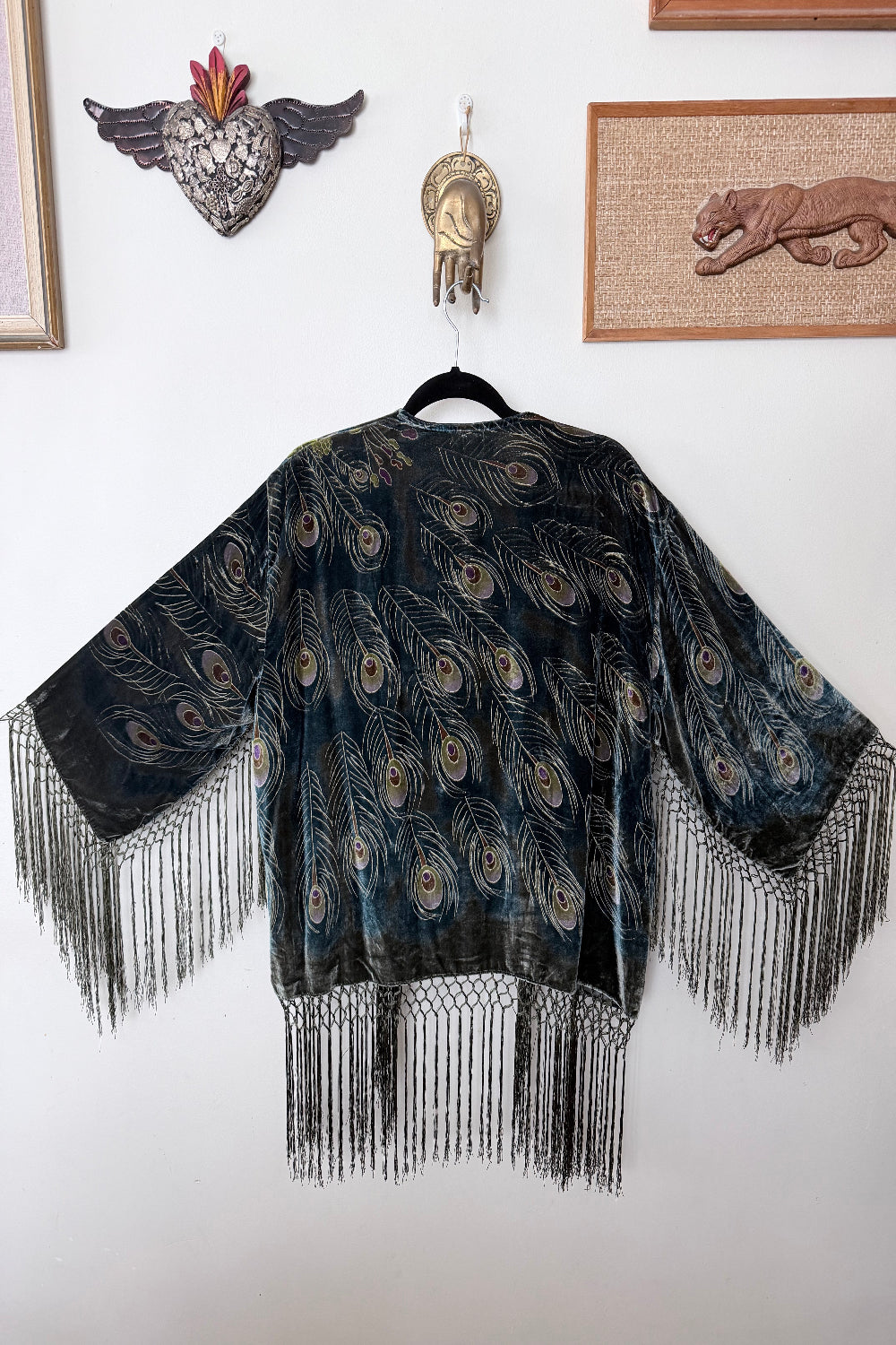 Peacock feather patterned jacket with fringes against a white wall.