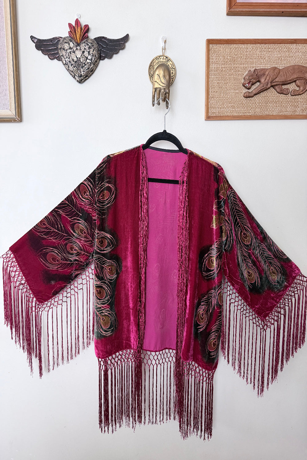 red velvet silk jacket with peacock feathers print hanging on a white wall