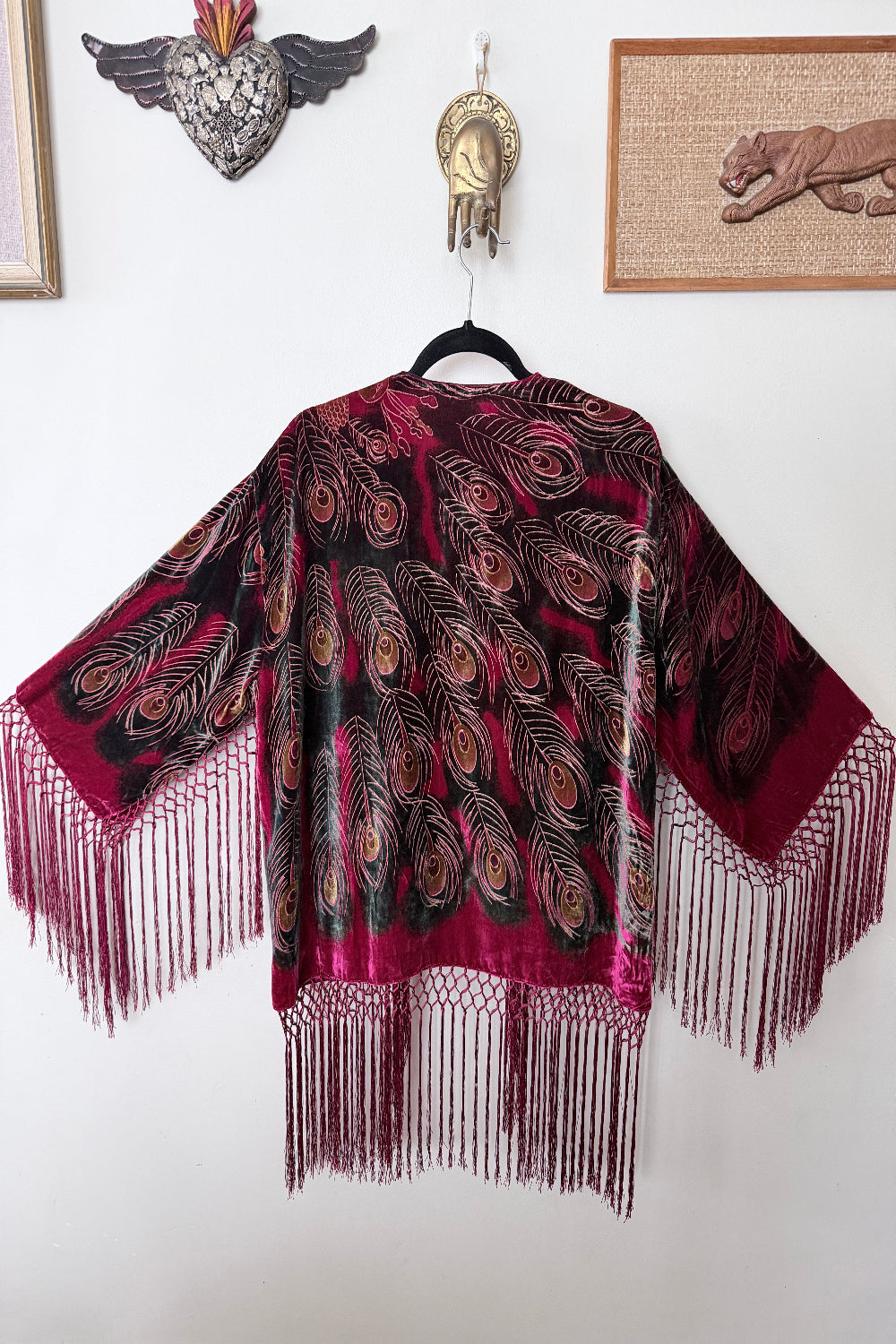Red velvet silk  jacket with peacock feathers and fringes on a white wall